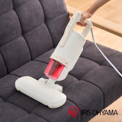 白色手持式除塵蹣機，配備紅色集塵筒，正用於清潔深灰色布藝沙發。