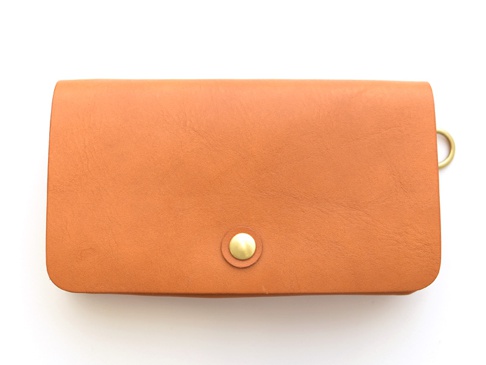 棕色皮革製成的旅行長夾，正面中央有一個金色按扣，右側有一個金色 D 型環。