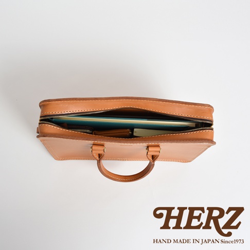 職人手作皮革公事包，淺棕色，拉鍊開口，內部可見文件夾、筆記本和錢包。