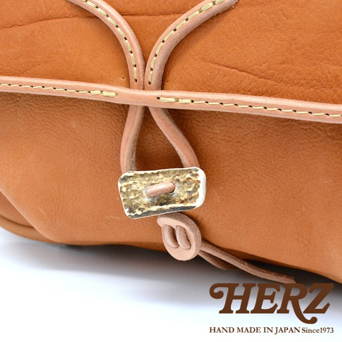 棕色皮革郵差包，採用鹿角扣環與皮革繩設計，搭配手工縫線，展現職人質感。