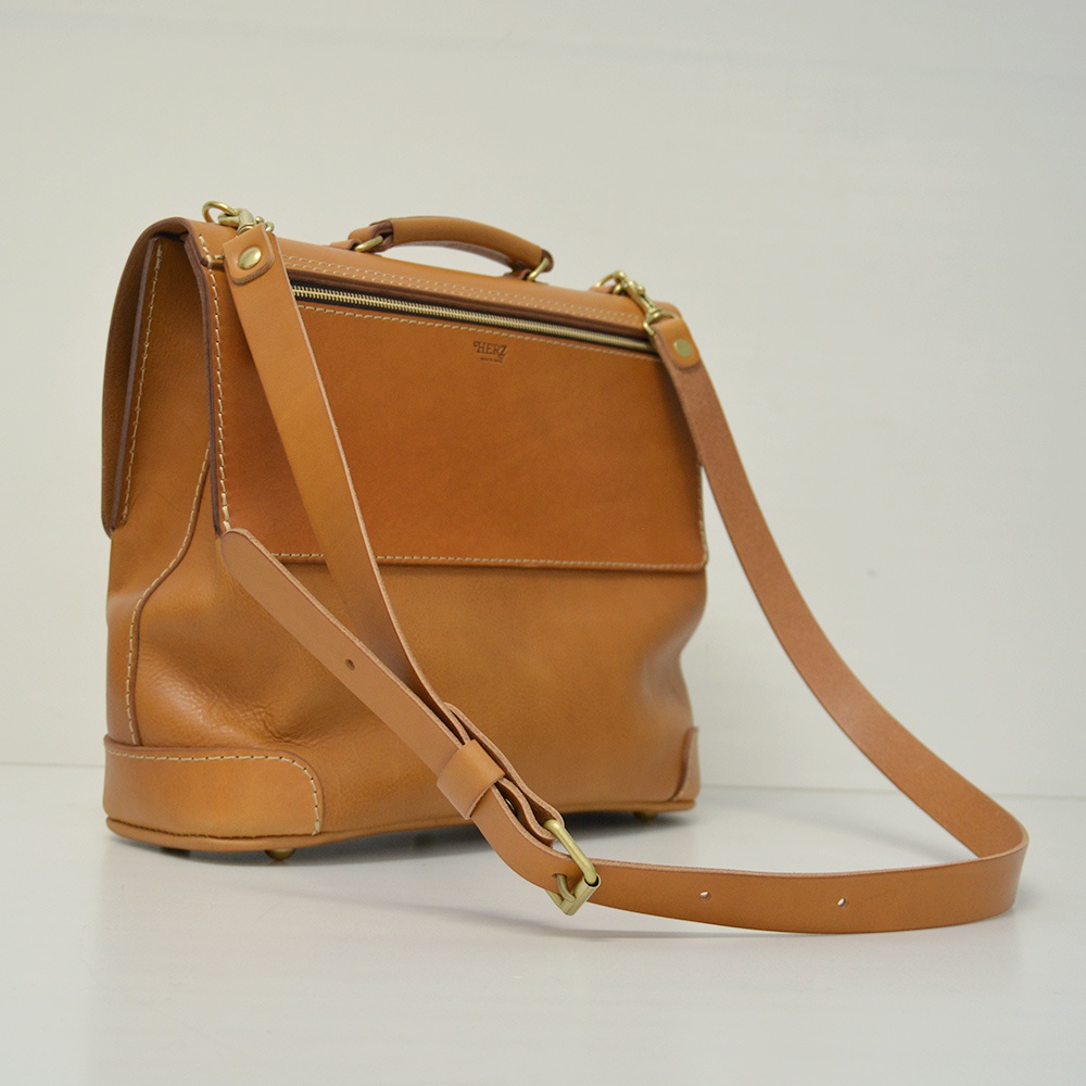 職人手作皮革旅行商務兩用波士頓包，採用天然棕色皮革，設有頂部提把、可拆卸肩背帶，以及金屬拉鍊與扣環。包身線條簡潔，結構紮實，展現皮革質感。