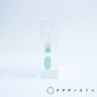 透明壓克力塊中垂直排列三顆片狀標本，由上至下依序為白色、淺藍色和綠松石色，呈現天然石材紋理。