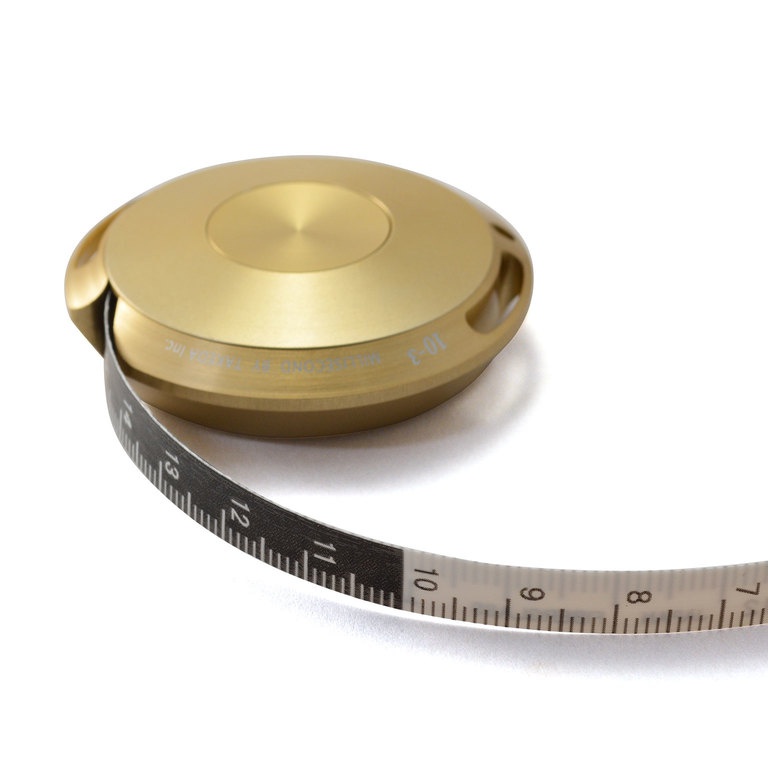 一個金色鋁製卷尺，帶有一個圓形外殼，上面刻有文字和數字，一條帶有黑色背景和白色刻度的軟尺從外殼中展開。