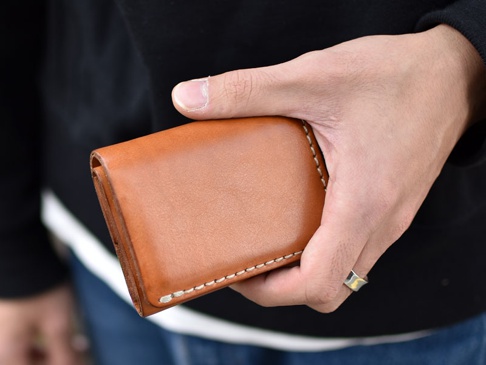 職人手作皮革三折式迷你短夾 (WS-2)，採用鞣製皮革材質，呈現經典棕色，以白色車縫線裝飾，設計簡潔。