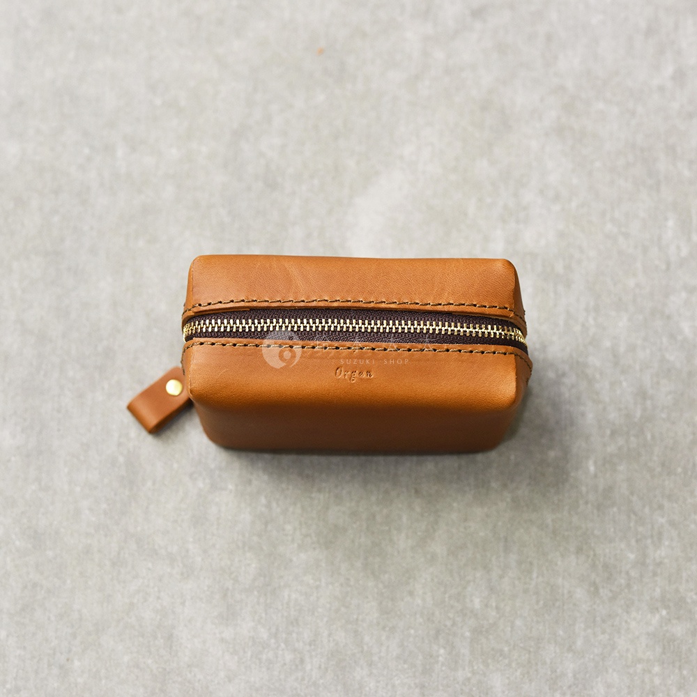 一個側視的棕色皮革箱型收納包，上面有拉鍊和一個小提把，中央印有 Organ 字樣。