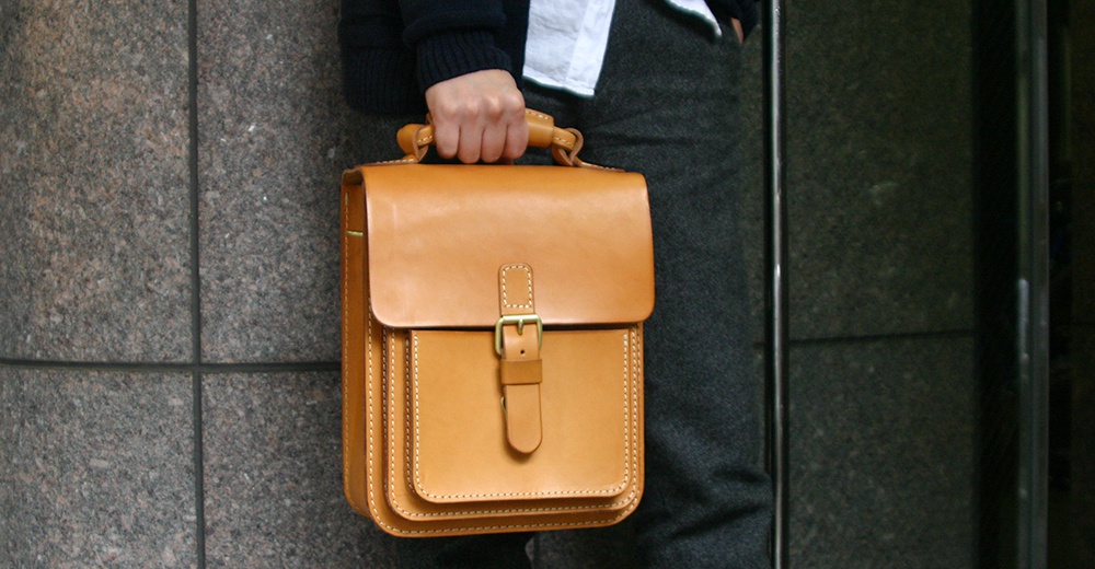 職人手作皮革單肩兩用小方包，呈現原色皮革光澤，配有金屬釦環和縫線細節。