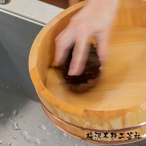 一隻手正在使用棕色天然毛刷清潔木製水桶的內部。