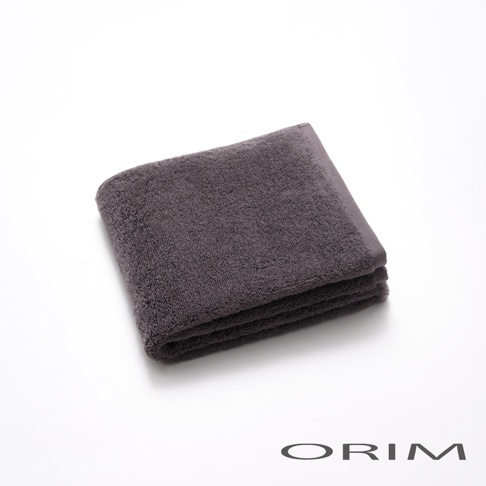 一條深灰色、觸感柔軟的毛巾，以對角線方式折疊，展示其細緻的織紋與邊緣。