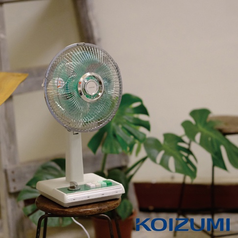 復古風格的白色桌上型電風扇，10吋金屬扇網，綠色扇葉，底座為白色搭配綠色按鈕與銀色旋鈕，放置於木製小圓凳上，背景為綠色植物。