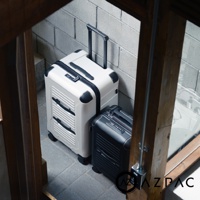 AZPAC 品牌標誌下方，兩個不同尺寸的行李箱，左邊為白色，右邊為黑色，擺放在磚牆前方的灰色地板上。