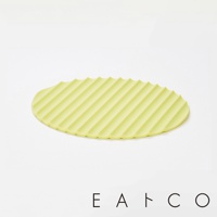 淡黃綠色橢圓形隔熱墊，表面有平行斜紋凹槽，邊緣呈波浪狀，材質為矽膠。