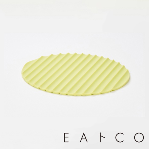 淡黃綠色橢圓形隔熱墊，表面有平行斜紋凹槽，邊緣呈波浪狀，材質為矽膠。