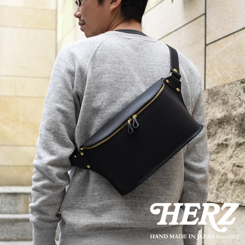 黑色皮革立體斜背包，搭配金色拉鍊與釦環，由日本HERZ品牌手工製作，展現職人技藝。