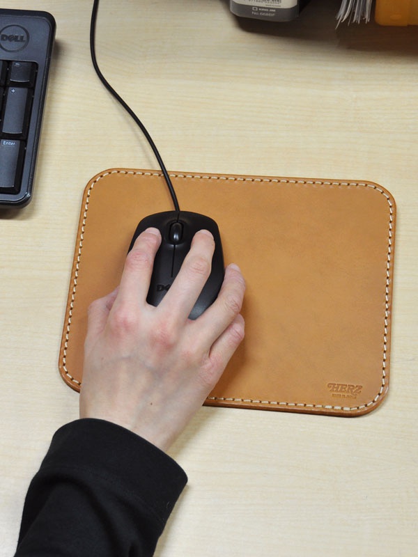 職人手作皮革滑鼠墊板 (KZ-70)，淺棕色皮革材質，邊緣縫線清晰，搭配黑色滑鼠，左手操作。